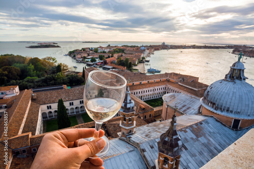 Glass of wine in hand of tourist watching the panorama of Venice, and Giudeca island with ancient cathedrals and canals