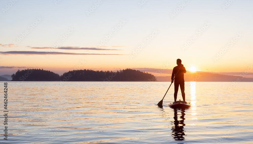 Adventurous Caucasian Adult Woman on a Stand Up Paddle Board is paddling on the West Coast of Pacific Ocean. Sunny Sunrise. Victoria, Vancouver Island, BC, Canada.
