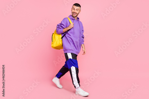 Full length photo of funky young brunet guy go wear hoodie pants shoes bag isolated on pink background