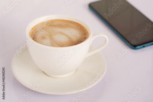 White latte coffee mug, side view on white desk and mobile phone