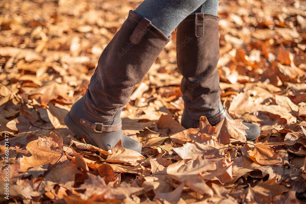 Boots of a woman walking through fallen leaves in autumn