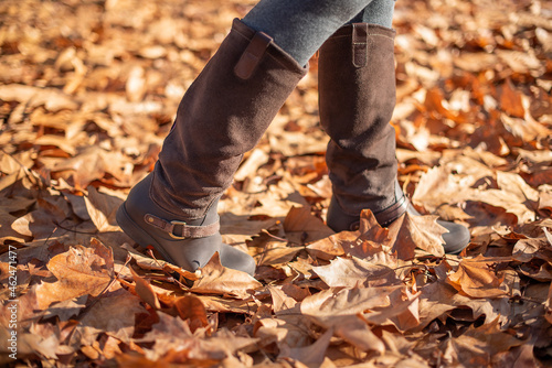 Boots of a woman walking through fallen leaves in autumn