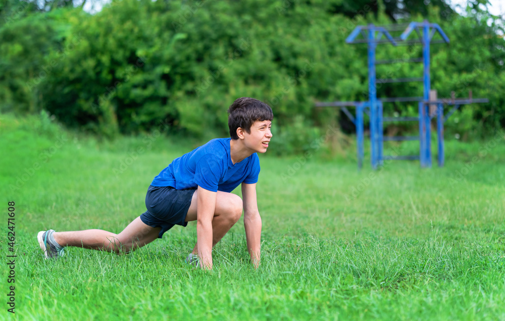 teenage boy exercising outdoors, sports ground in the yard, he squats and does a warm-up, healthy lifestyle teenage boy exercising outdoors, sports ground in the yard, he squats and does a warm-up, healthy lifestyle