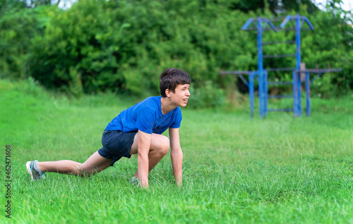 teenage boy exercising outdoors, sports ground in the yard, he squats and does a warm-up, healthy lifestyle