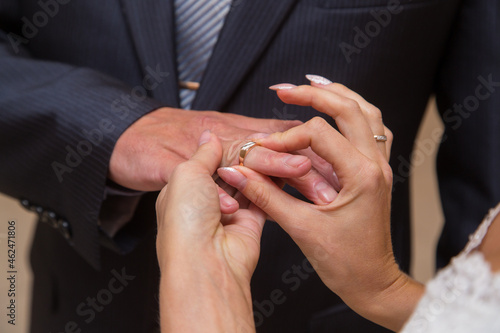 The bride's girlfriend's hands put a ring on her husband's ring finger. Large, close. The man in the jacket.