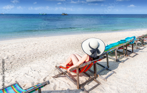 Asian woman sitting on a beach chair wearing a white sun hat.