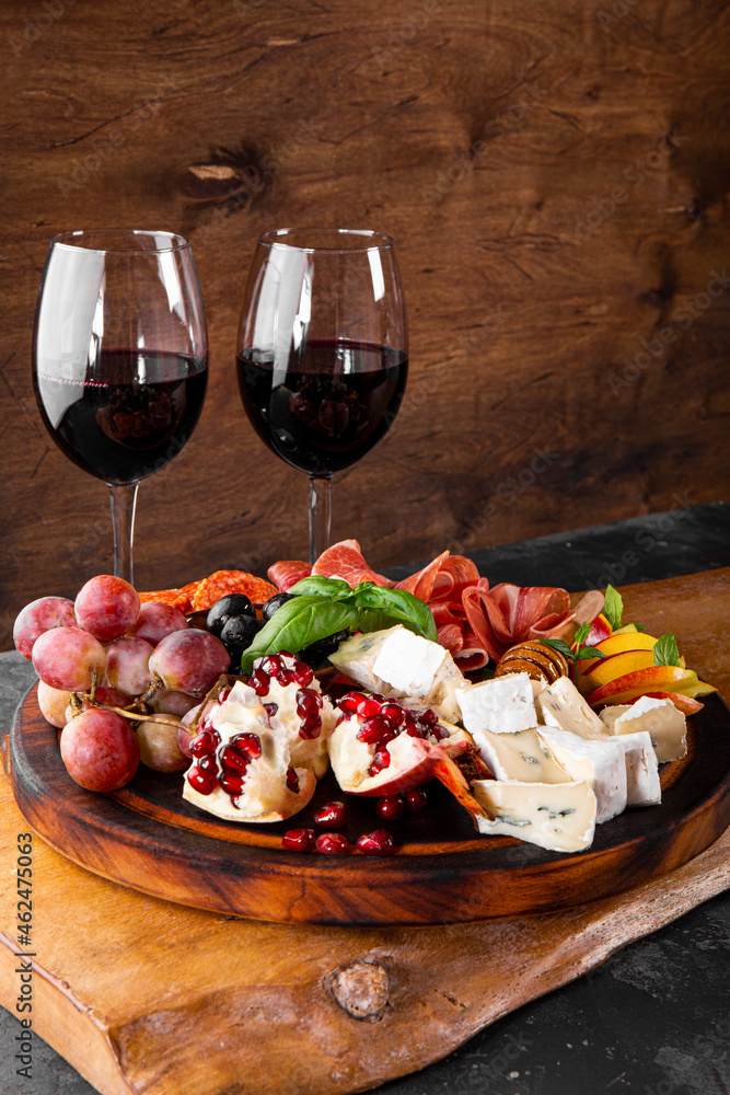  A set of appetizers for wine, jamon, pepperoni, cheese, grapes, peach and olives on the table. Snack board and two glasses of red wine vertical photo