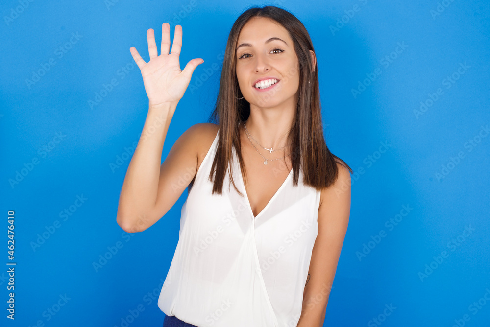 Young european brunette woman wearing white T-shirt on blue background showing and pointing up with fingers number five while smiling confident and happy. Young european brunette woman wearing white T-shirt on blue background showing and pointing up with fingers number five while smiling confident and happy.