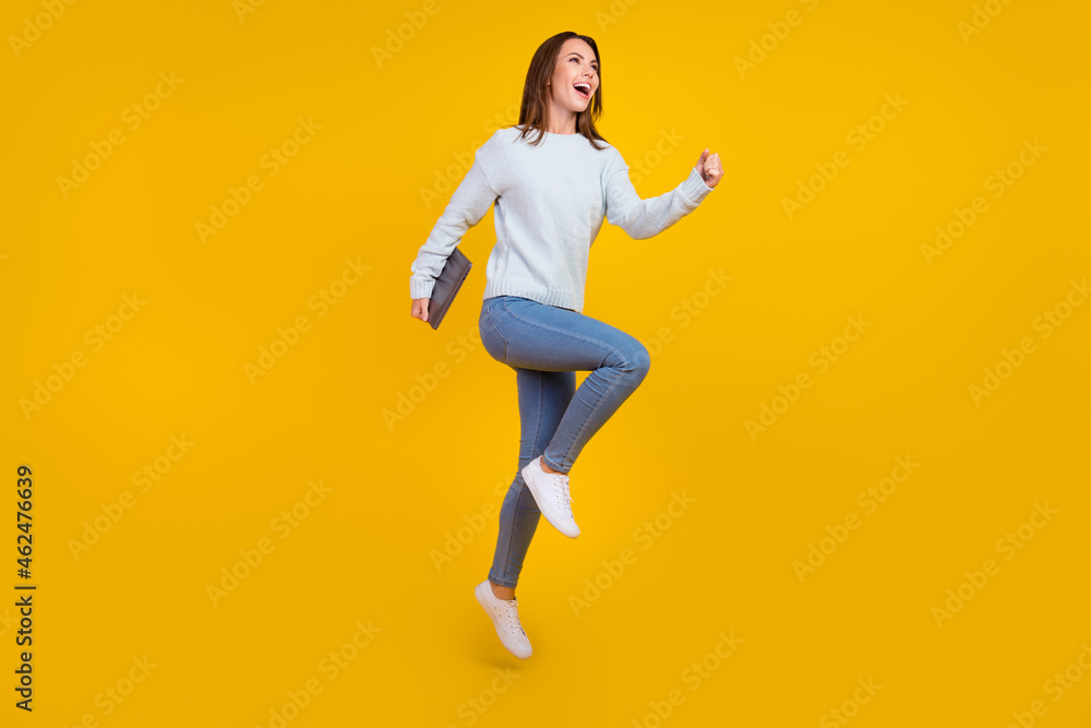 Full body photo of brunette haired stylish trendy lady hold laptop run empty space jump isolated on yellow color background
