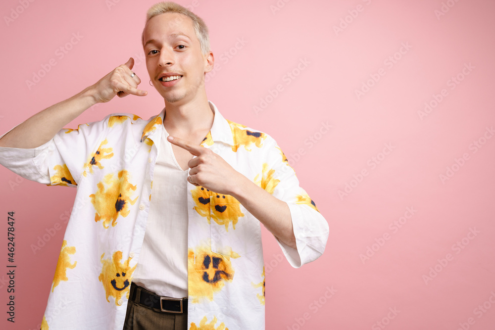 Young blonde man pointing finger aside and making handset gesture Young blonde man pointing finger aside and making handset gesture
