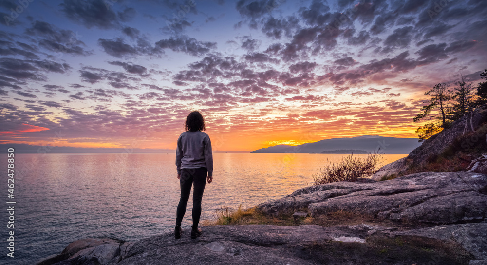 Caucasian Woman on a rocky coast during a dramatic cloudy sunset. Lighthouse Park ,Horseshoe Bay, West Vancouver, British Columbia, Canada. Adventure Travel Concept