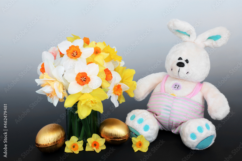 Easter bunny with golden eggs, daffodil flowers in a vase. Symbols of Easter and Spring fun concept on gradient grey background.