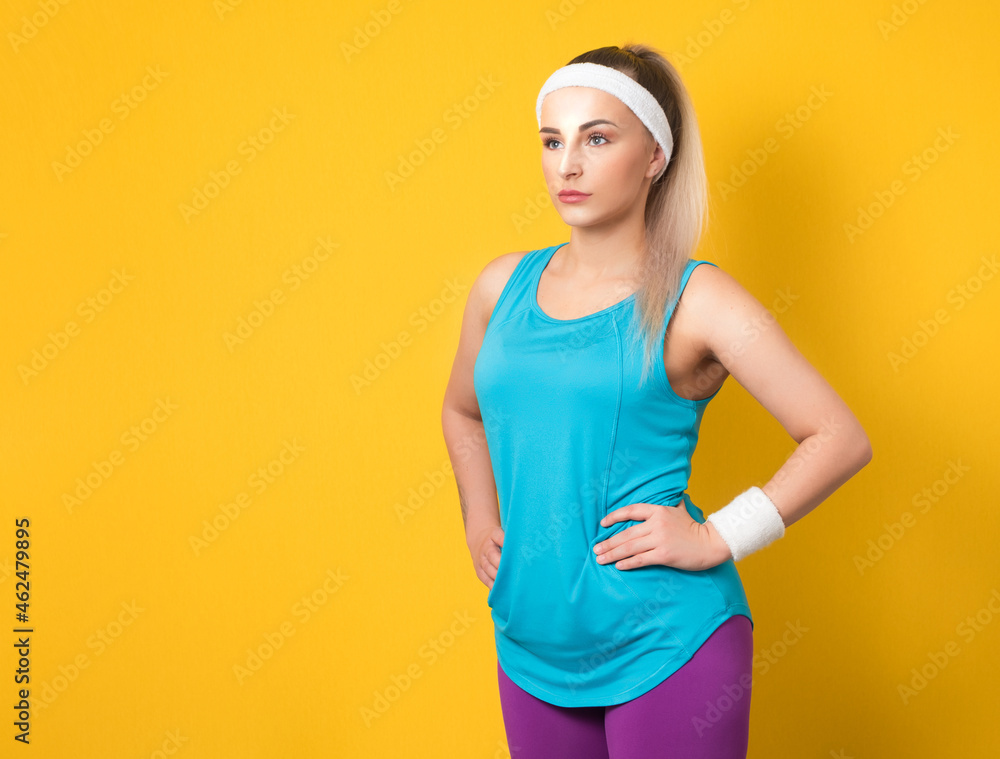 Fitness young woman posing and looking to side, isolated on yellow background. Half length of sportswoman ready for exercising. Athletic female person. 80s styling Fitness young woman posing and looking to side, isolated on yellow background. Half length of sportswoman ready for exercising. Athletic female person. 80s styling