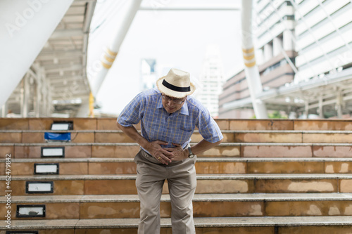 Asian elderly man tourist having abdominal painful outdoor. Asian senior man standing alone and suffering having abdominal pain outdoor