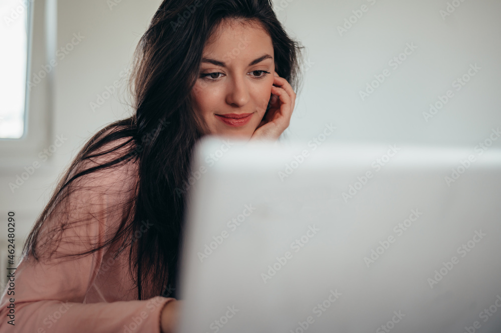 Beautiful young woman wearing a pajama and using a laptop while working from home