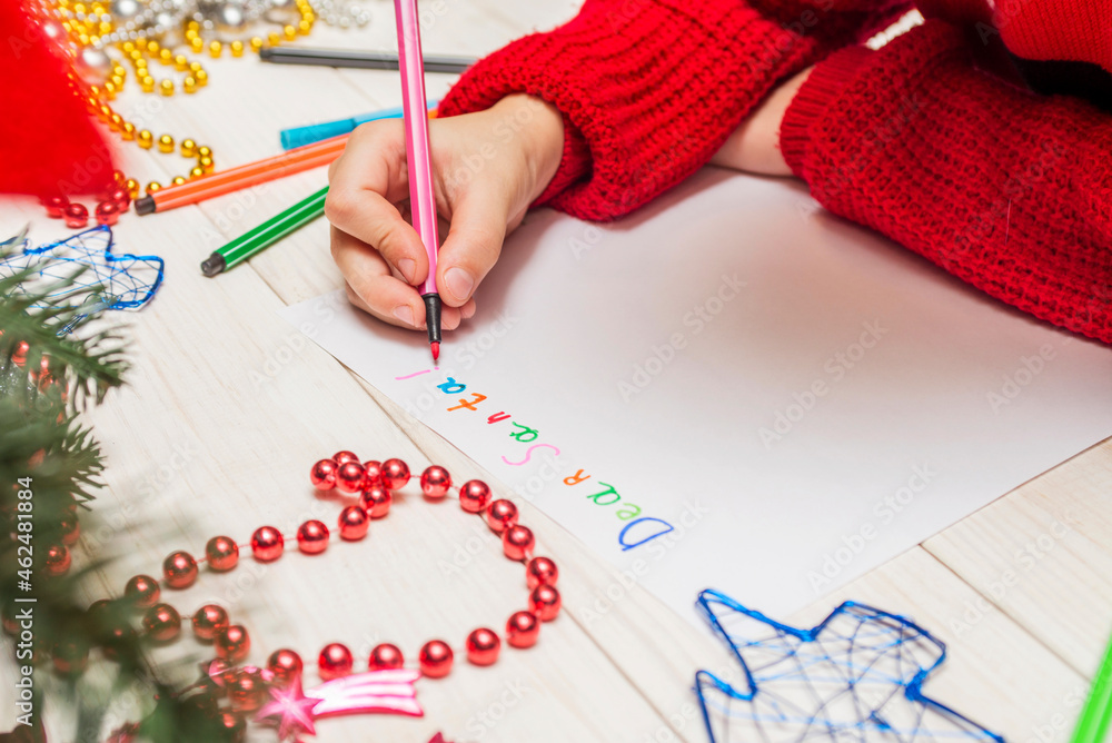 Little boy in writes letter to Santa Claus. Kid in Santa hat writing wish list Little boy in writes letter to Santa Claus. Kid in Santa hat writing wish list