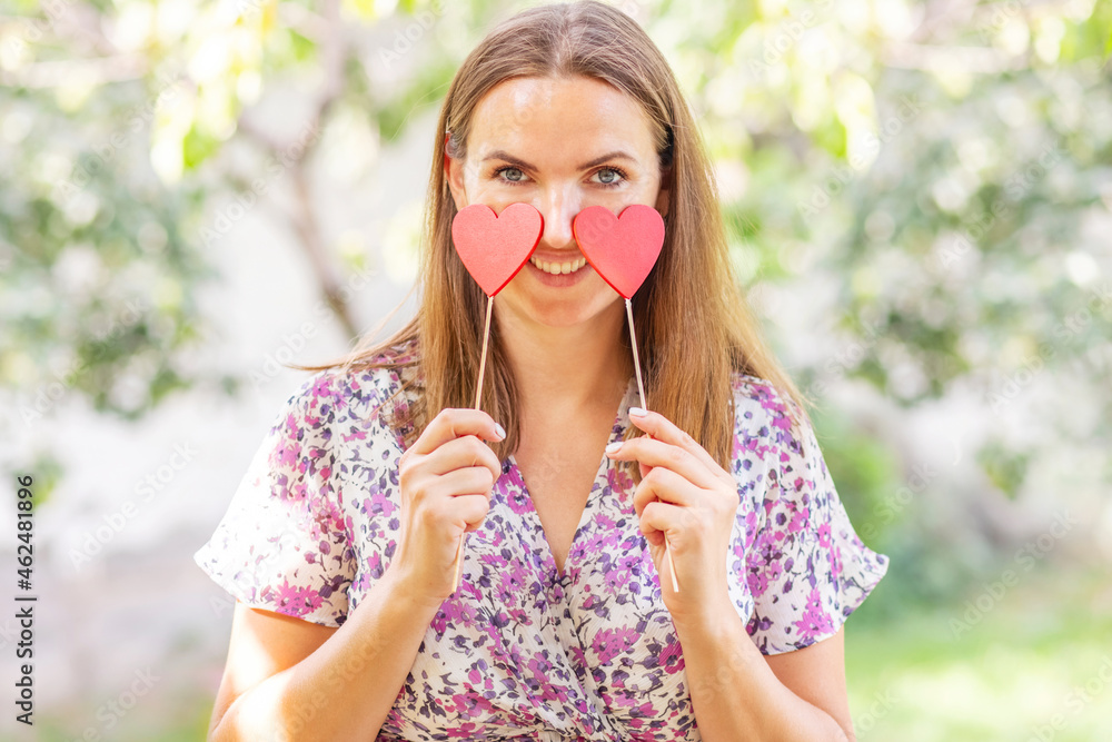 Happy beautiful woman with two decorative hearts in her hands is smiling on the natural backround Happy beautiful woman with two decorative hearts in her hands is smiling on the natural backround