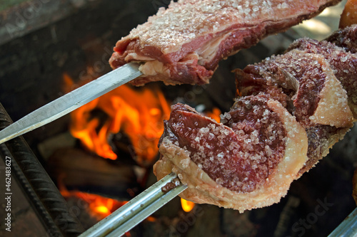 Seasoned raw rump steak and pork on the grill with fire, the traditional Churrasco Gaúcho, Brazilian barbecue made outdoors.