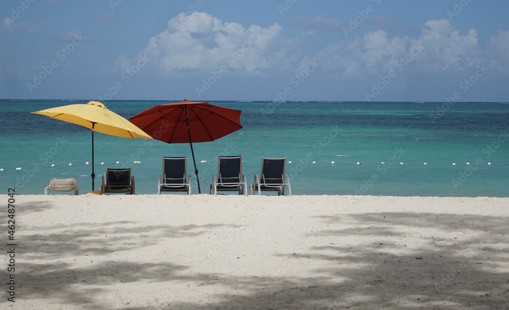Fototapeta premium Tropical secluded beach with red and yellow umbrellas and chairs overlooking the ocean