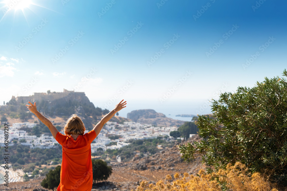 A blonde woman looks at the panorama of Lindos on the island of Rhodes, Greece A blonde woman looks at the panorama of Lindos on the island of Rhodes, Greece