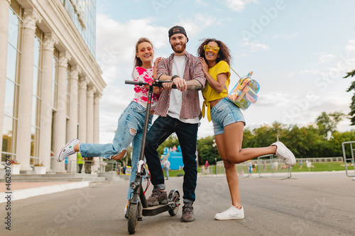 happy young company of smiling friends walking in street with electric kick scooter