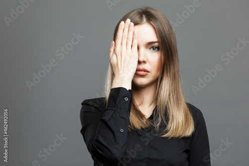 The young woman covered one eye with her hand. Beautiful blonde in a black shirt. Conspiracy theory and Masonic symbolism. Gray background. photo