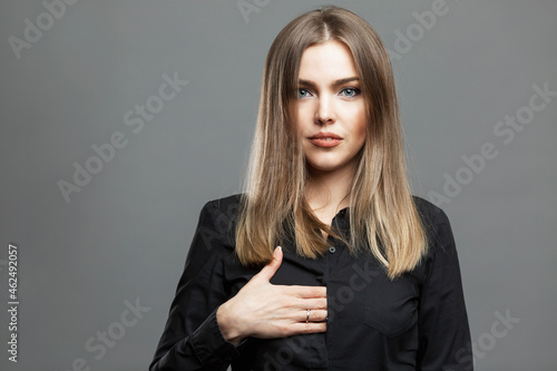 Young woman shows a hidden hand sign. Beautiful blonde in a black shirt. Masonic symbolism and the theory of the world conspiracy. Gray background.