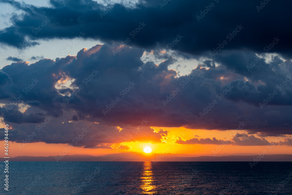 Stunning dramatic, cloudy sunrise with a bright sun rising over a calm water. Natural background, Sardinia, Italy.