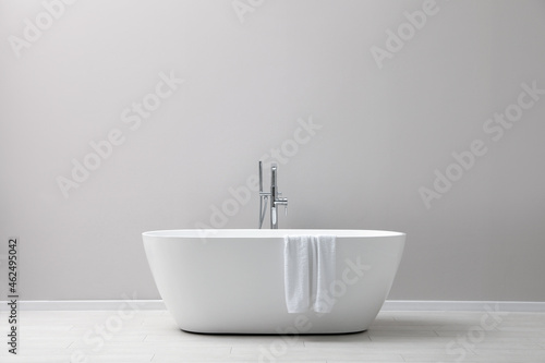 Fotografia Modern ceramic bathtub with towel near light wall indoors
