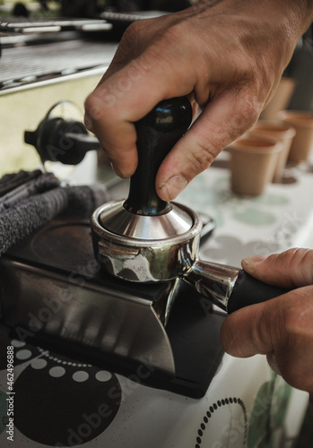 Barista preparing coffee in coffee machine with equipment - vertical photo. Closeup of coffee making process. Hands of barista using a coffee machine.