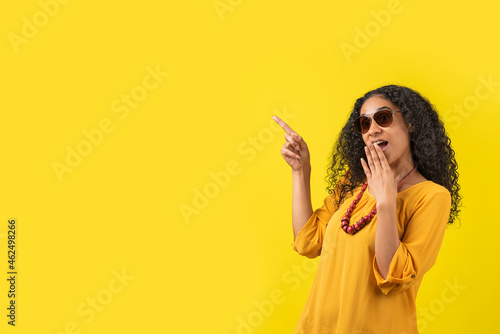 Fotografia Mujer afroamericana asombrada señalando a un lado en un fondo amarillo