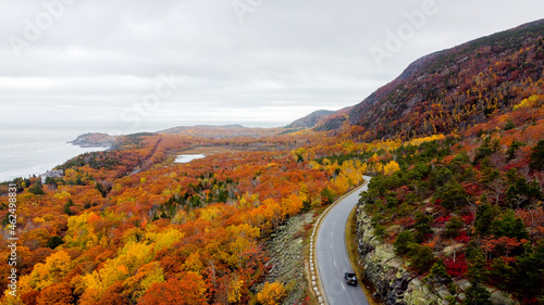 Aerial view of fall or autumn foliage in maine - drone view of coastline and road - orange and red leaves and foliage - mountains and hills