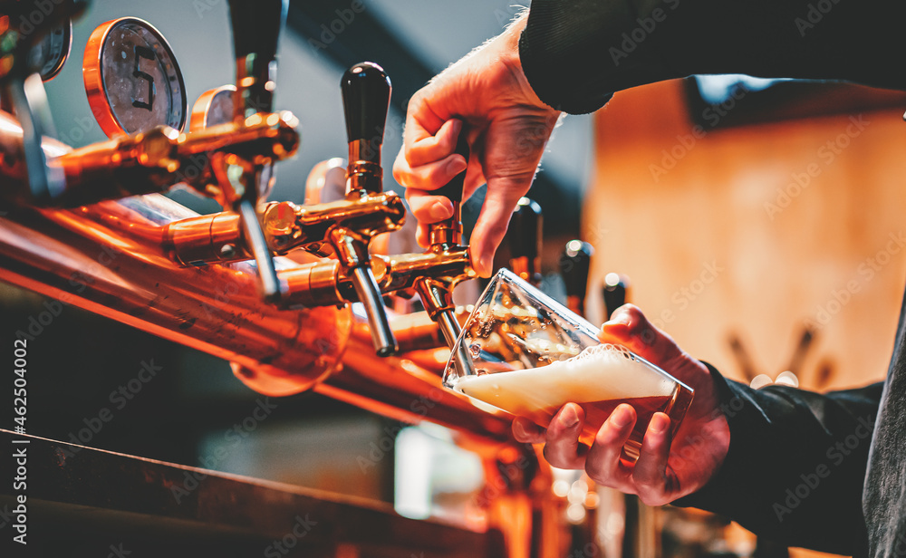 bartender hand at beer tap pouring a draught beer in glass serving in a ...