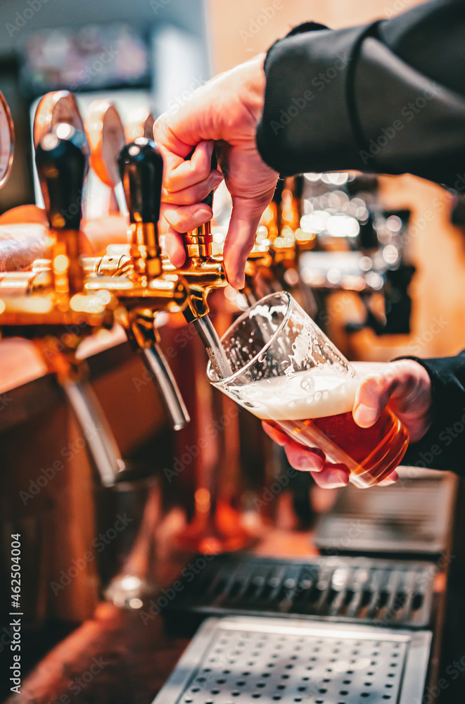 bartender hand at beer tap pouring a draught beer in glass serving in a ...
