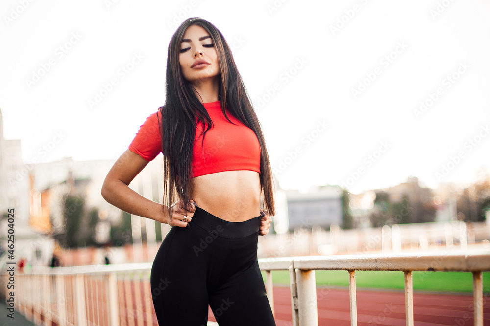 Beautiful fitness woman in sportswear posing near running track.