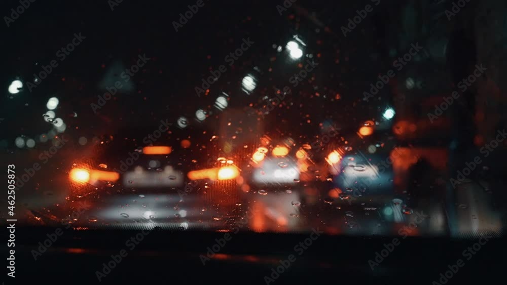 Wet car window with working brushes when driving through a traffic jam in the rain late at night. Wet car window with working brushes when driving through a traffic jam in the rain late at night.