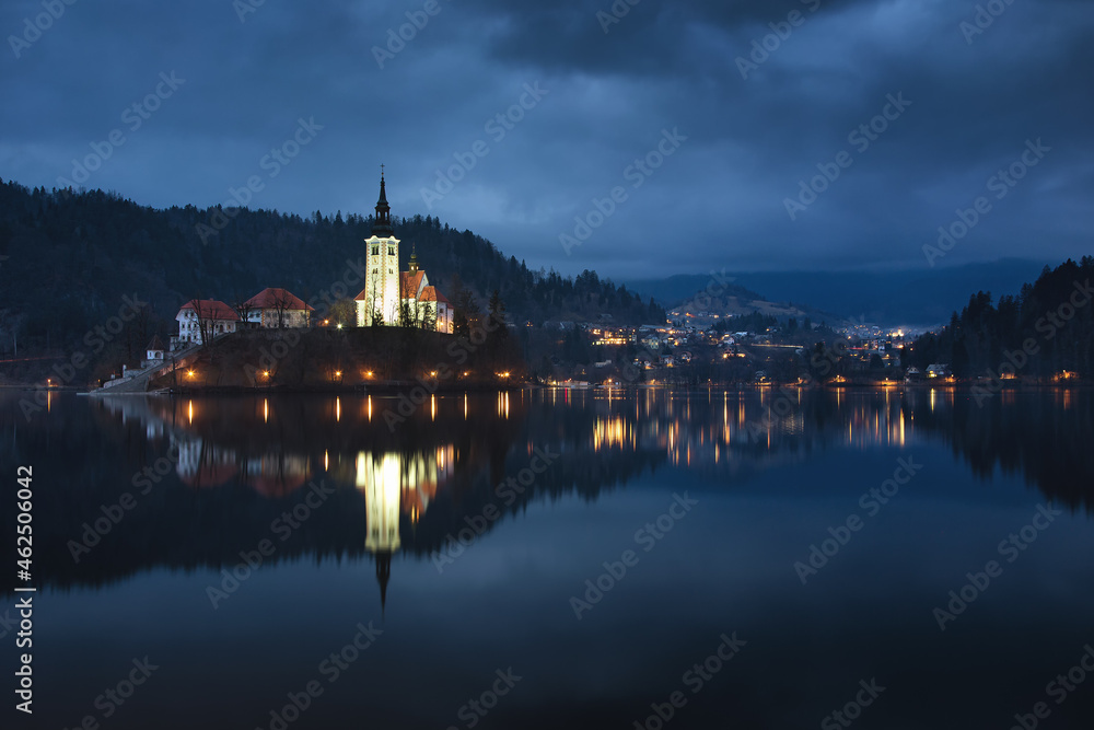A mysterious evening view of Lake Bled, Slovenia. Landscape with the lights of the city at night. Church on an island, postcard view, national park.