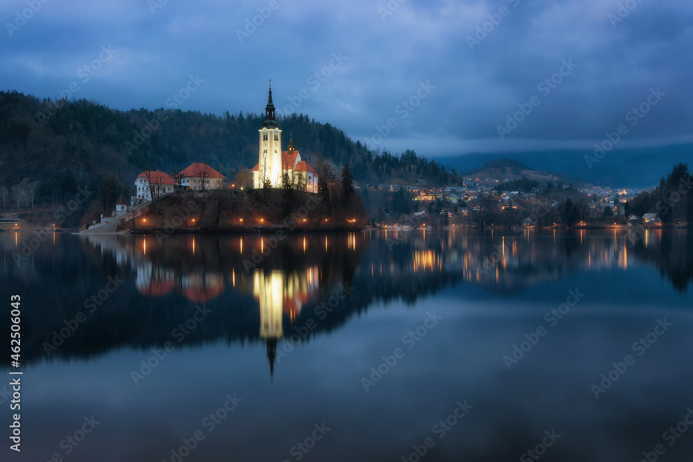 A mysterious evening view of Lake Bled, Slovenia. Landscape with the lights of the city at night. Church on an island, postcard view, national park, Julian Alps.