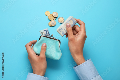 Woman putting money into wallet on blue background photo