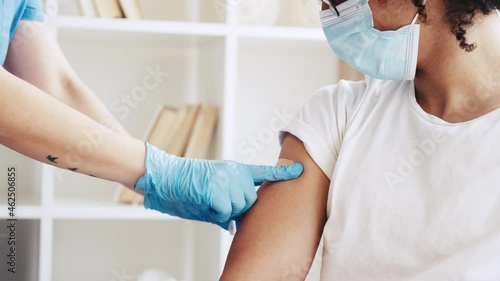 Coronavirus vaccine. Flu shot. Pandemic prevention. Female doctor in gloves sticking plaster after covid-19 jab to Arab male patient shoulder. photo