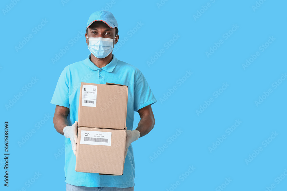 African-American delivery man in medical mask and with parcels on color background African-American delivery man in medical mask and with parcels on color background