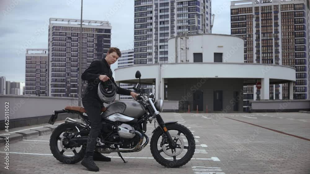 Young man wears helmet and starts scrambler motorbike on top of the multi-level parking in city. Guy starting cafe racer in empty parking garage. High quality 4k footage Young man wears helmet and starts scrambler motorbike on top of the multi-level parking in city. Guy starting cafe racer in empty parking garage. High quality 4k footage