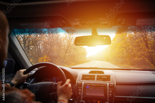man driving a car on an autumn road at sunset. Close-up of hands on a steering wheel. view from the driver's back. empty road. view from the car