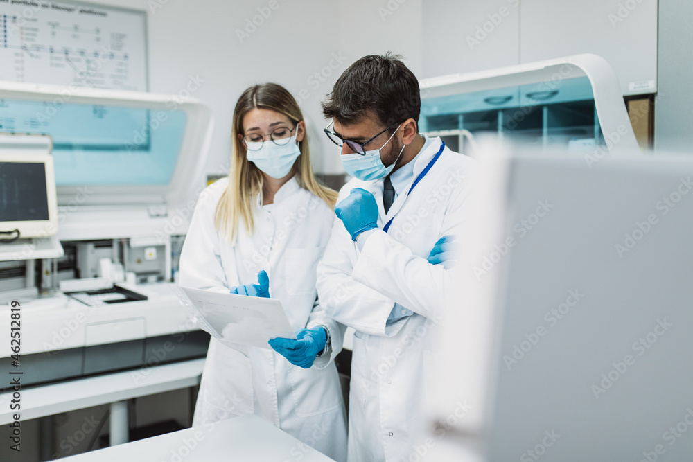 Two scientists or technicians with face protective masks work in laboratory on human blood samples. Two scientists or technicians with face protective masks work in laboratory on human blood samples.