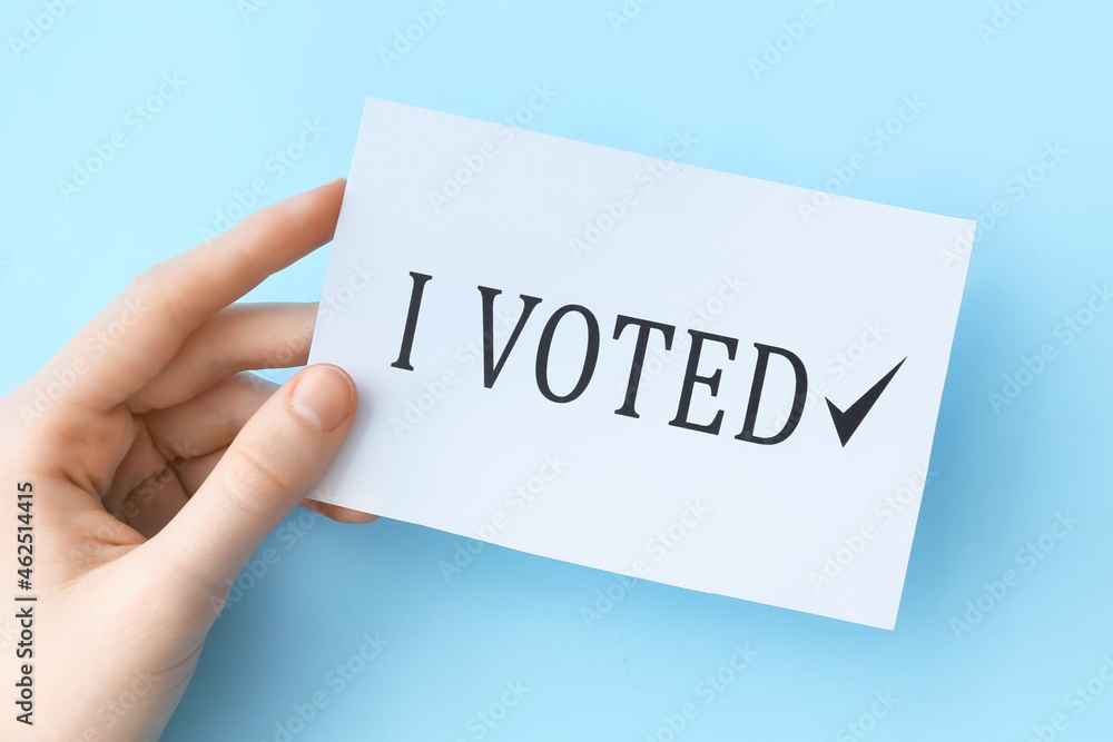 Hand holding paper with text I VOTED on color background Hand holding paper with text I VOTED on color background