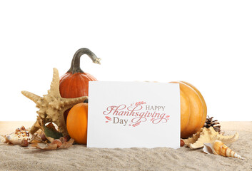 Pumpkins, starfish, seashells and card with text HAPPY THANKSGIVING DAY on sand against white background