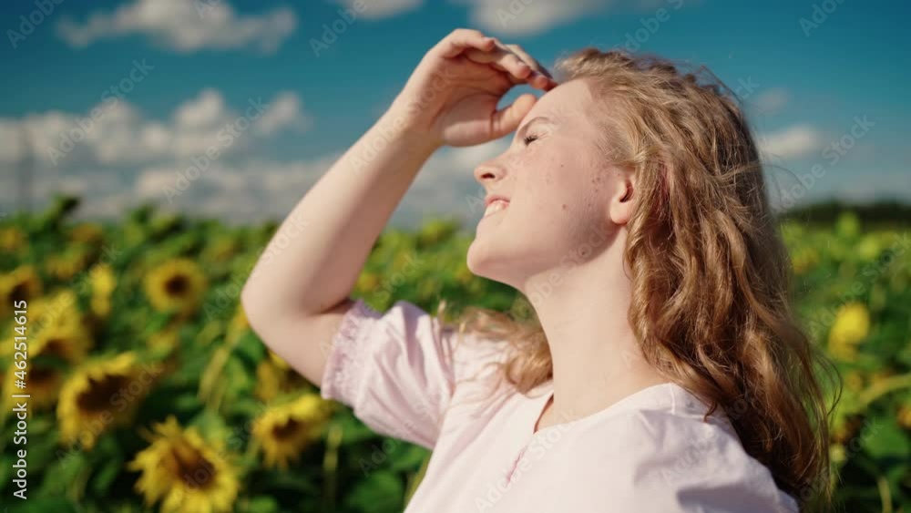 young beautiful pretty blonde caucasian girl in a long light dress in a sunflower field on a sunny day shyly smiles, straightens her curly hair, looks at the sun, squints, covers himself with his hand young beautiful pretty blonde caucasian girl in a long light dress in a sunflower field on a sunny day shyly smiles, straightens her curly hair, looks at the sun, squints, covers himself with his hand
