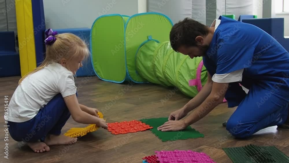 Child with therapist assembles massage mat for sensory integration lesson. Foot massage to prevent flat feet in children and relieve tension Child with therapist assembles massage mat for sensory integration lesson. Foot massage to prevent flat feet in children and relieve tension