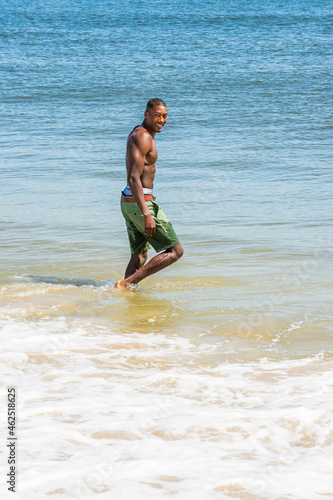 Obraz na płótnie A well built young sexy black guy, half naked, is walking on water of ocean, turning back, smiling. . w salonie