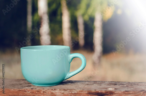 A cup of tea stands on a wooden table against the background of nature. Space for text, copy-space.